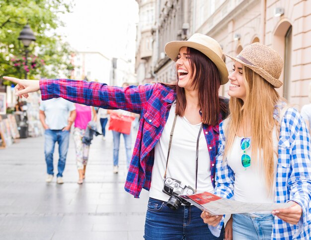 Woman showing something to her happy female friends holding map