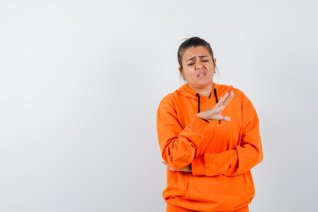 woman showing stop gesture in orange hoodie and looking dissatisfied