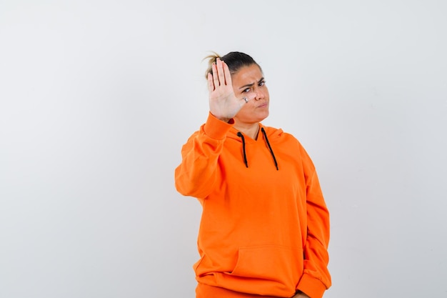 woman showing stop gesture in orange hoodie and looking serious