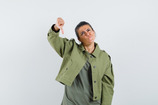 woman showing thumb down in jacket, t-shirt and looking hesitant