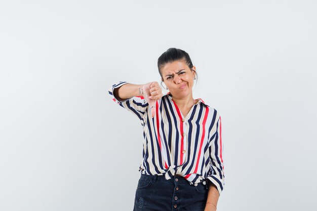 woman showing thumb down in shirt, skirt and looking displeased