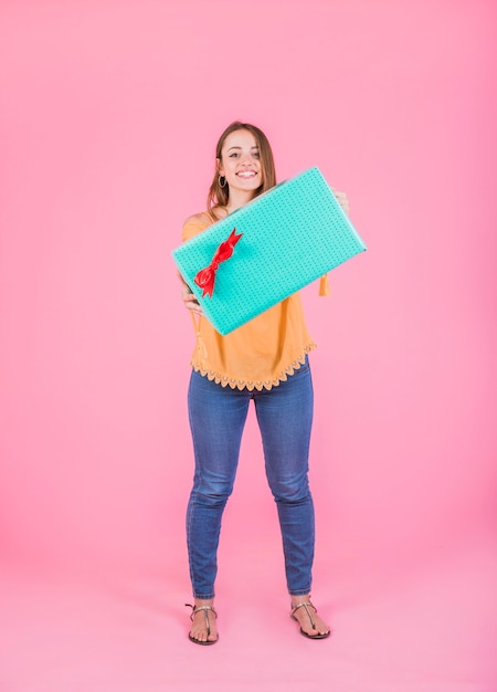 Woman showing wrapped gift box standing against pink background