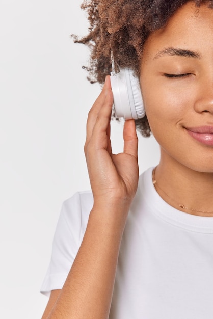 woman shows half of face keeps hands on stereo headphones enjoys favorite melody dressed in casual t shirt isolated on white listens relaxing music