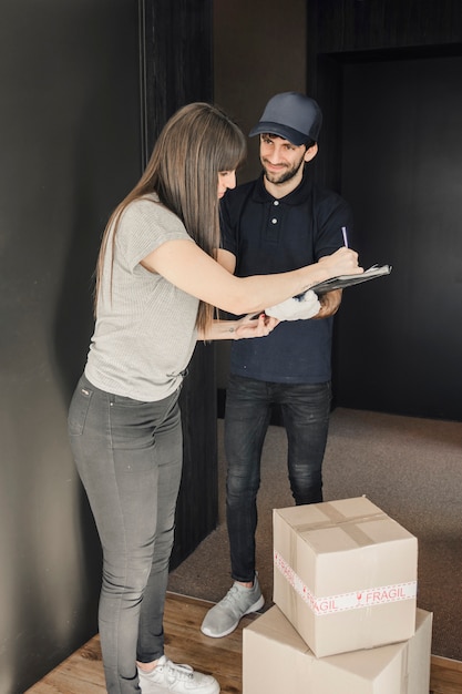 Woman signing on clipboard after parcel delivered by delivery man