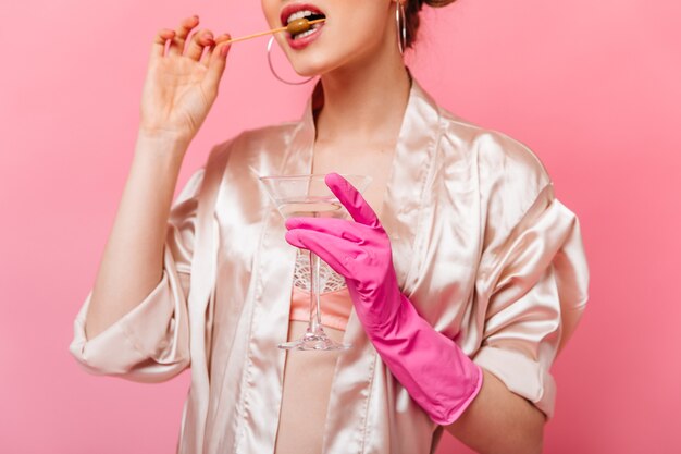 woman in silk robe and rubber gloves eating olive and holding martini glass