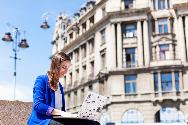 Woman sits on the street and works with a laptop