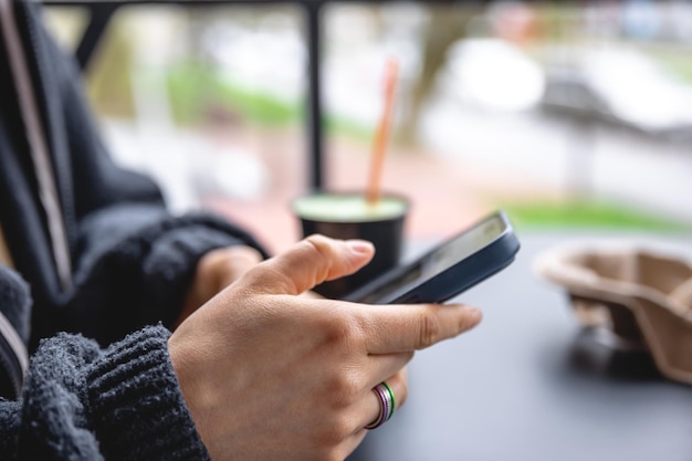 Una donna si siede sulla terrazza di un caffè e utilizza un primo piano dello smartphone