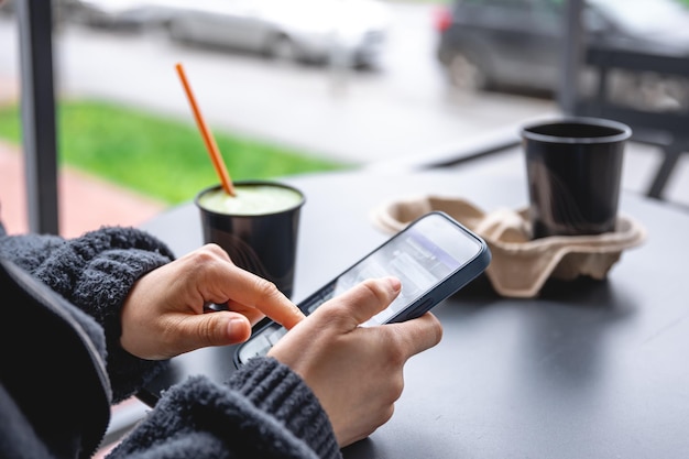 Una donna si siede sulla terrazza di un caffè e utilizza un primo piano dello smartphone