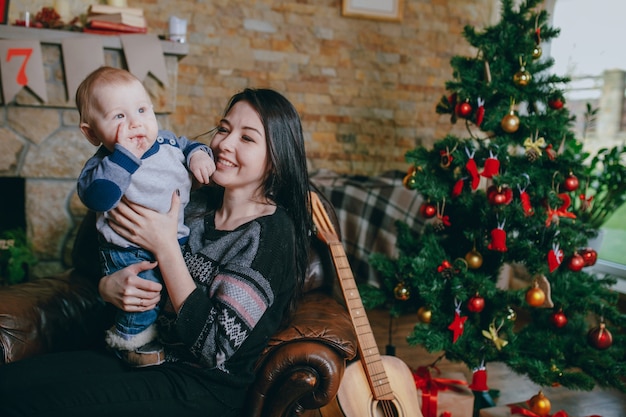 Foto gratuita donna seduta in una poltrona con il suo bambino e una chitarra accanto ad essa