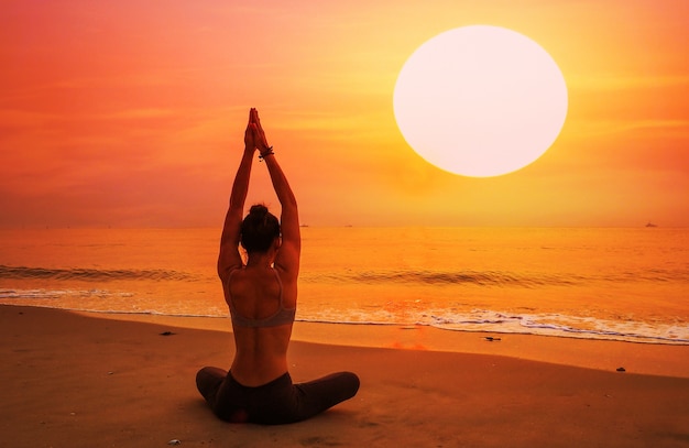 Woman sitting on a beach with arms stretched