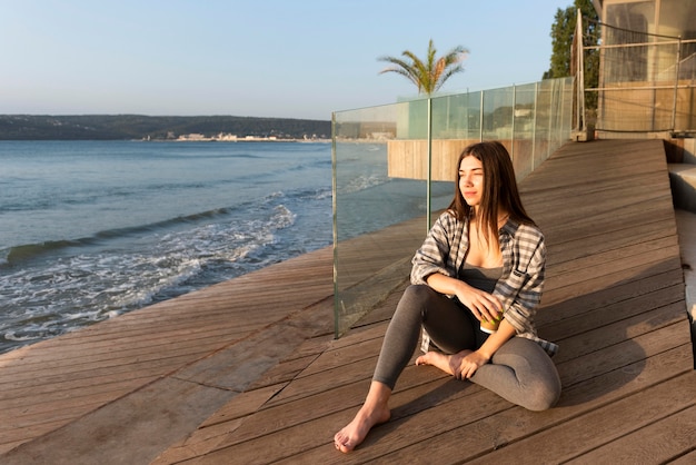 Free photo woman sitting next to the beach with copy space