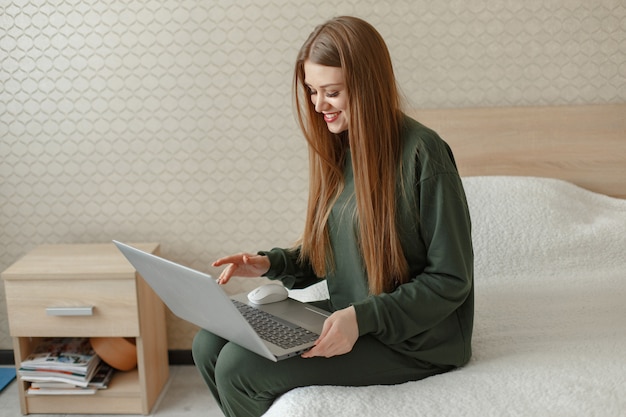 Donna seduta su un letto e utilizza un computer portatile