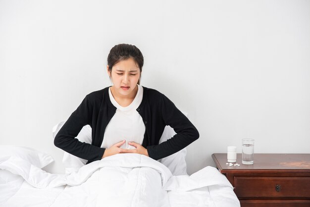 A woman sitting in bed with abdominal pain and pressing her hand on her stomach.