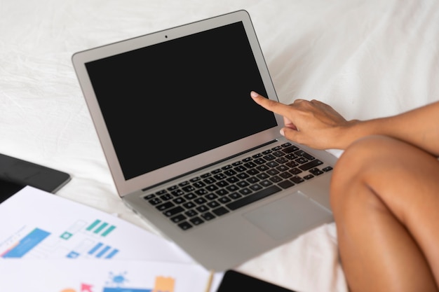 ノートパソコンと書類とベッドに座っている女性