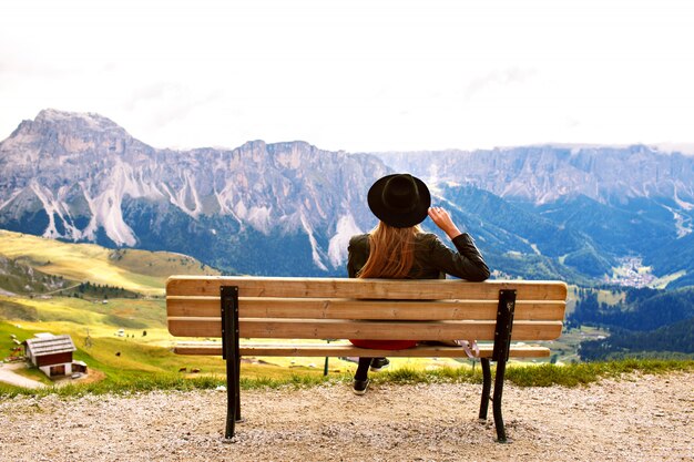 ドロミテの巨大な山々の景色を楽しみながらベンチの端に座っている女性