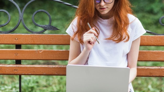 Foto gratuita donna che si siede sul banco con laptop e penna