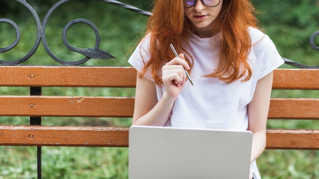 Donna che si siede sul banco con laptop e penna