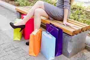 Free photo woman sitting on bench with multi colored shopping bags
