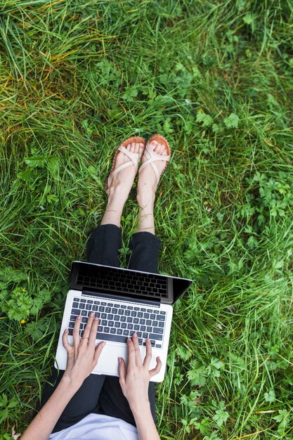 Женщина, сидя на яркой траве с ноутбуком
