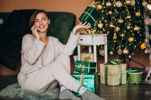 Woman sitting by Christmas tree and shopping on the phone