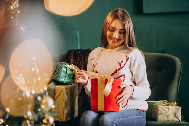 クリスマスツリーのそばに座って、クリスマスプレゼントを開梱する女性