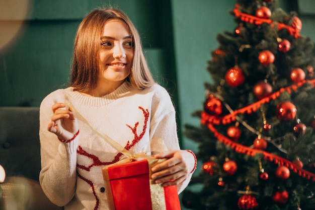 Woman sitting by Christmas tree and unpacking christmas present