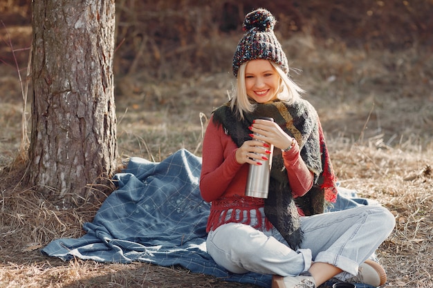 woman sitting by a tree in a spring forest with a drink thermos