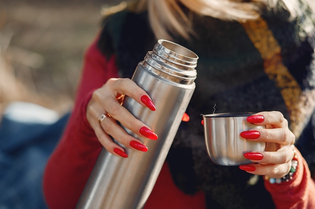 woman sitting by a tree in a spring forest with a drink thermos