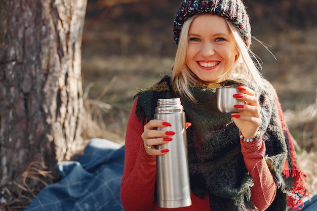 woman sitting by a tree in a spring forest with a drink thermos