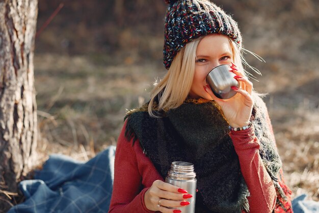 woman sitting by a tree in a spring forest with a drink thermos