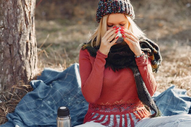 woman sitting by a tree in a spring forest with a drink thermos