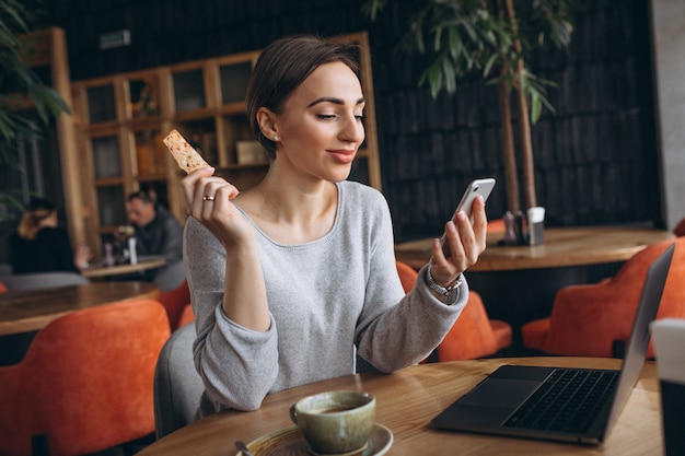 Donna che si siede in un caffè bevendo caffè e lavorando su un computer