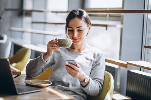 Женщина, сидя в кафе, пить кофе и работает на компьютере
