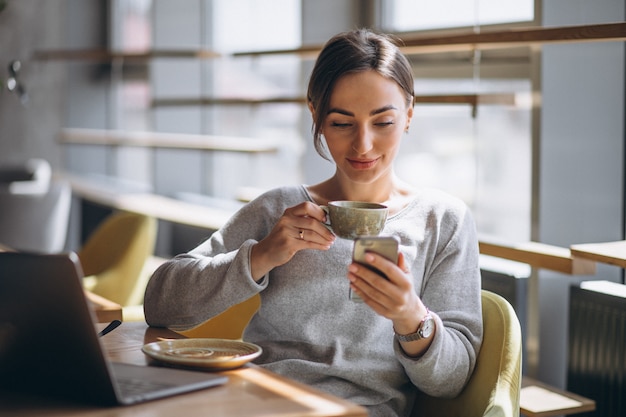 コーヒーを飲みながら、コンピューターに取り組んでいるカフェに座っている女性