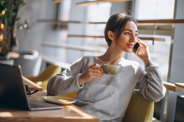 コーヒーを飲みながら、コンピューターに取り組んでいるカフェに座っている女性