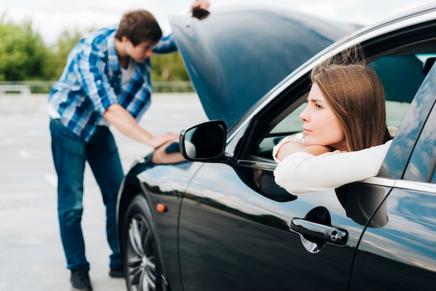 Woman sitting in car while man checks engine