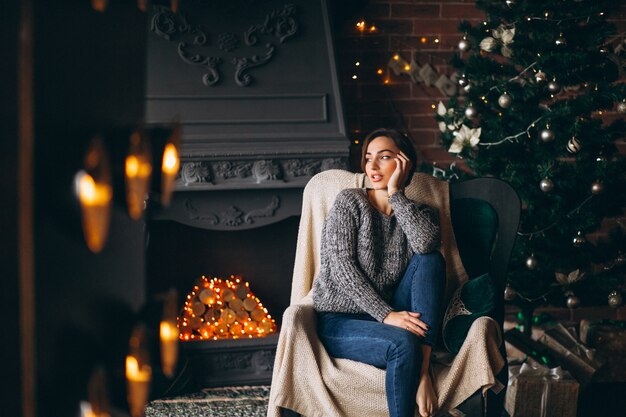 Woman sitting in chair by Christmas tree