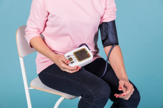 Woman sitting on chair checking blood pressure on electric tonometer