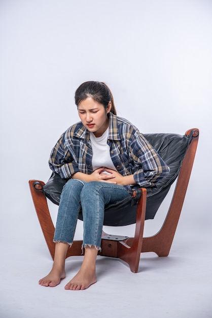 A woman sitting in a chair with abdominal pain and pressing her hand on her stomach