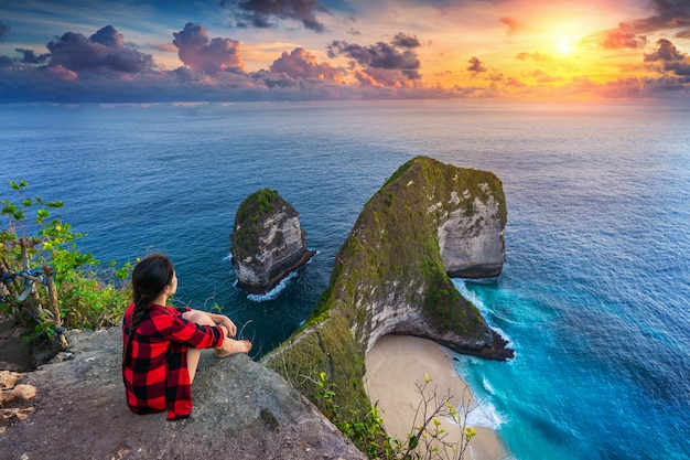 여자 절벽에 앉아 누사 페니 다 섬, 발리, 인도네시아의 Kelingking 해변에서 일몰을보고