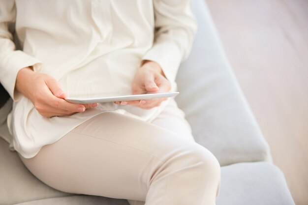 Женщина, сидящая на диване и использующая планшет