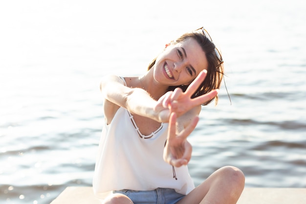 Woman sitting on dock doing the peace sign