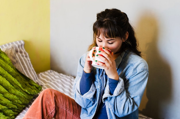 Woman sitting and drinking on bed