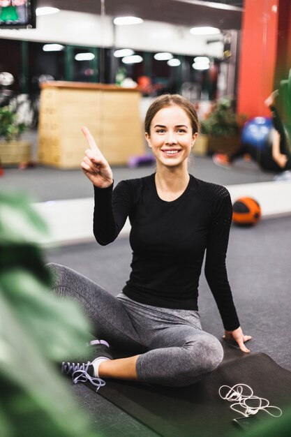 Woman sitting on exercise mat pointing upwards