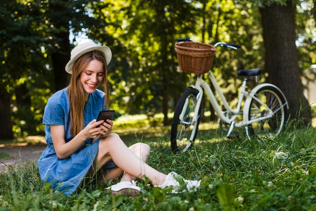 Женщина сидит на траве, проверяя ее телефон