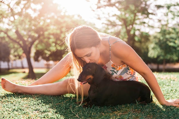 Woman sitting on green grass kissing her dog at park