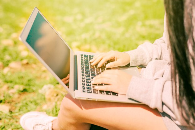 Женщина сидит на зеленой траве и работает в ноутбуке