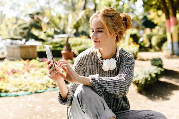 温室に座っている女性が自分の携帯電話で自分撮りをします