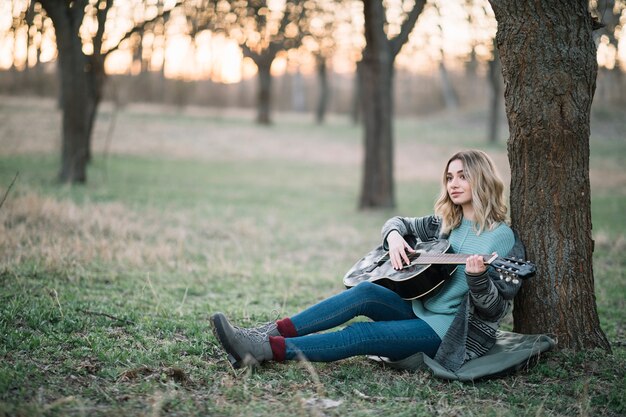 Женщина сидит на земле с гитарой