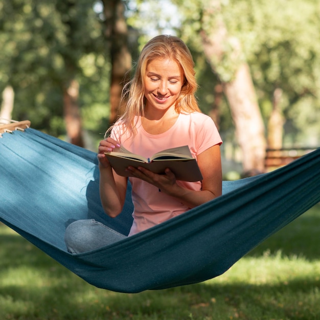 Free photo woman sitting in hammock and reads